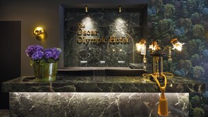 A reception desk with a marble top, a vase of purple flowers, and a wall with a tree mural. - The Oscar Olympic Hotel (Thessaloniki)