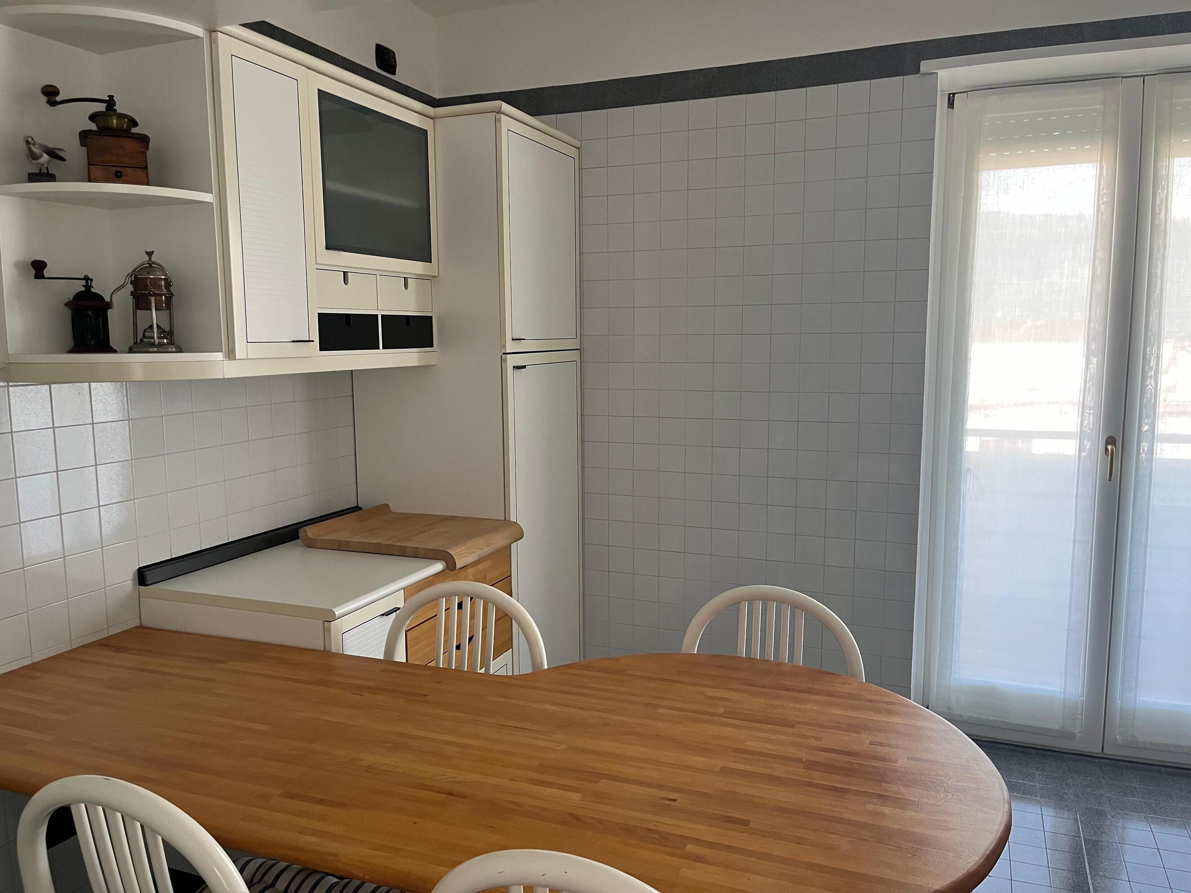 Une cuisine avec des meubles blancs, une table en bois et deux chaises.