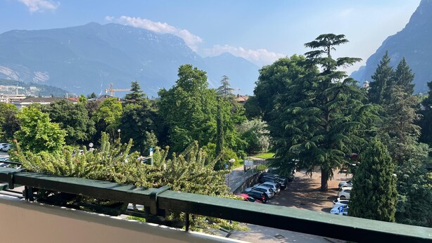 Un espace de stationnement avec des voitures, des arbres et des montagnes en arrière-plan.