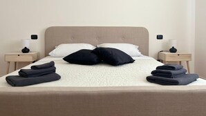 Un lit bien fait, avec une tête de lit beige, deux tables de chevet avec des lampes et des serviettes pliées posées sur le lit.