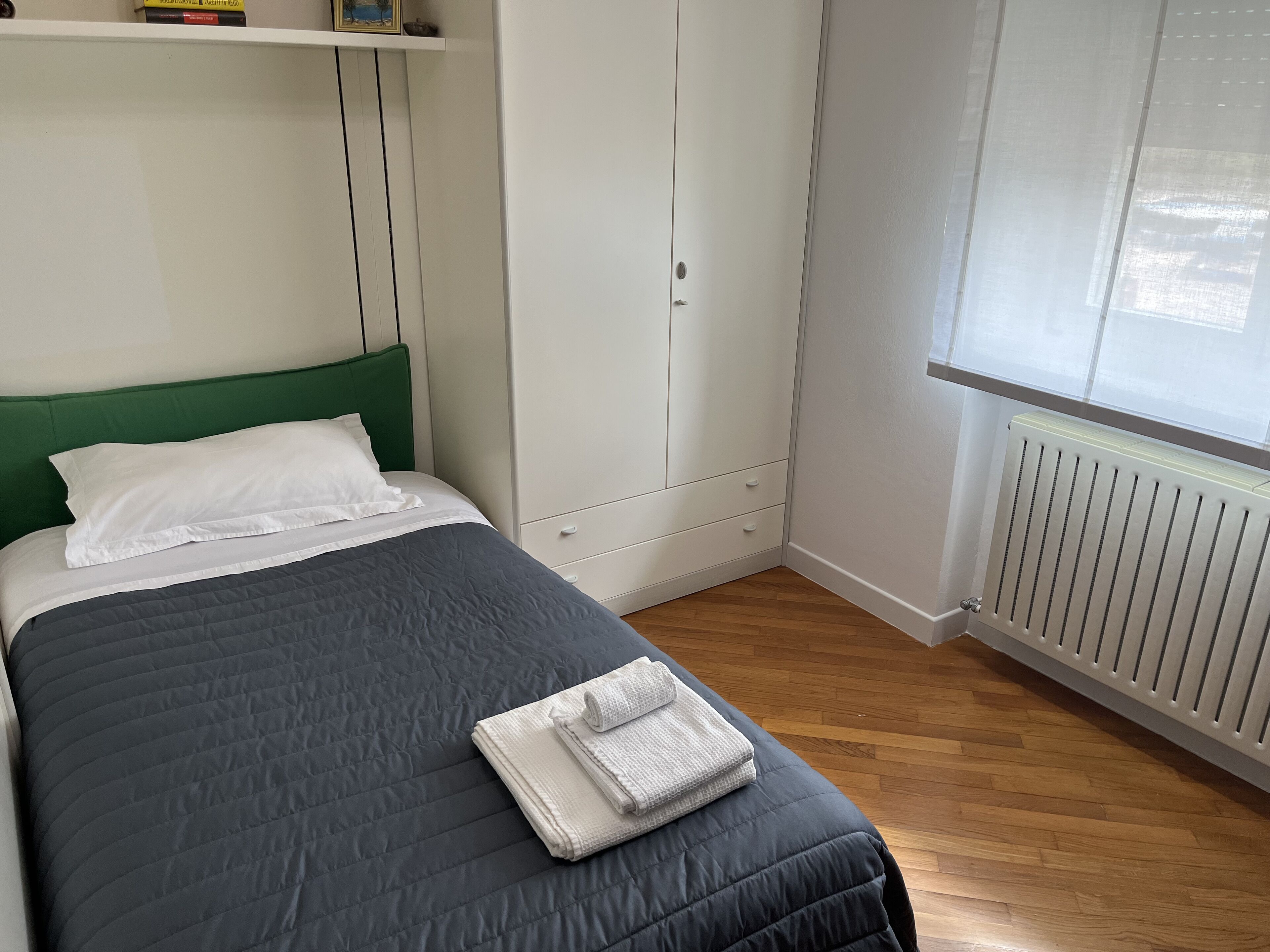 Un lit bien fait, avec une couverture grise, des oreillers blancs et une serviette pliée posée sur le pied de lit.