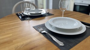 Une table à manger dressée avec des assiettes, des couverts et un verre à vin, avec une vue sur l’extérieur en arrière-plan.