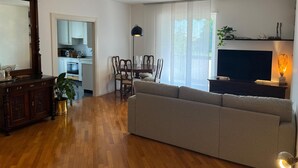 Un salon avec un canapé, une table à manger entourée de chaises, un téléviseur et, au fond, une cuisine.