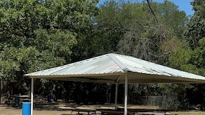 A covered picnic area with benches and a blue trash bin.