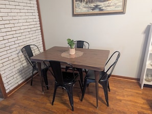 A dining area with a wooden table, four chairs, a small potted plant, and a framed picture on the wall.