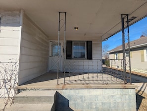 A covered porch with a metal railing, a door with a window, and a brick base.