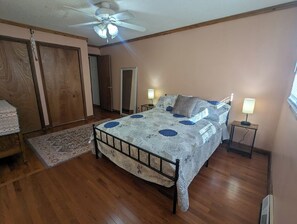 A bedroom with a bed, two bedside tables with lamps, a ceiling fan, and a wooden floor.