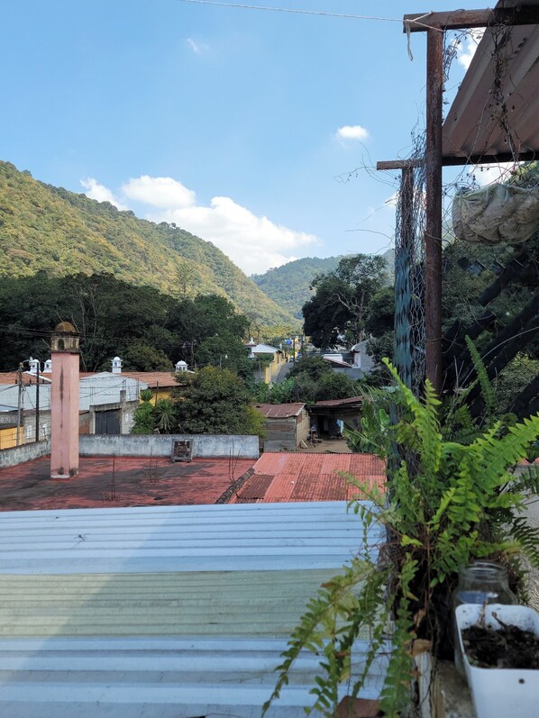Terraço com telhado vermelho, guarda-corpo branco e vista para uma paisagem montanhosa.