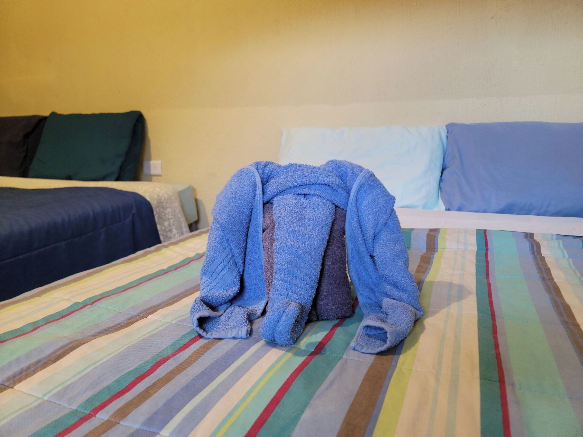 Una cama con un edredón a rayas, una manta azul y una almohada.