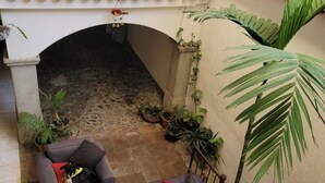A courtyard with two grey sofas, a red ottoman, and potted plants.