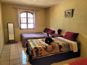 Una habitación con dos camas, una ventana con cortinas, un cuadro enmarcado en la pared y un espejo de pie.