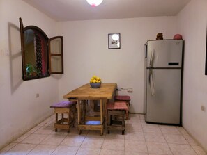 A small kitchen with a wooden table, two stools, a refrigerator, and a window with a decorative mirror. - Castillo De Los Gigantes (Antigua Guatemala)