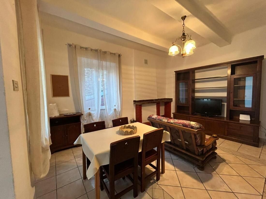 Zona pranzo con tavolo, sedie, divano, televisore e un mobile.