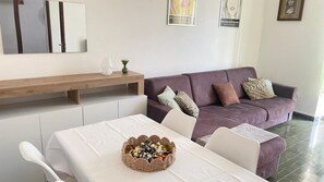 Ein modernes Wohnzimmer mit einem violetten Sofa, einem Esstisch mit weißem Tischlein und einem dekorativen Korb auf dem Tisch.