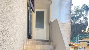 Unos escalones de piedra conducen a una puerta, con un muro de hormigón a un lado y un edificio con andamios al otro.