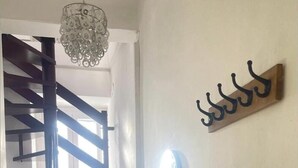 Una escalera con barandilla de madera y un candelabro. Hay un perchero en la pared y un espejo redondo.