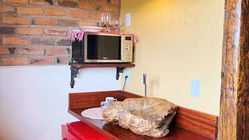 Una cocina compacta con pared de ladrillo, microondas, refrigerador rojo y mostrador de madera.
