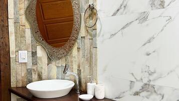 A bathroom with a stone mosaic wall, a wooden vanity, a white sink, a mirror, and a toilet.