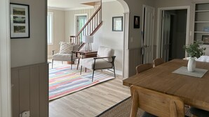 A spacious living area with a wooden dining table, two armchairs, a colorful rug, and a staircase leading to another room.