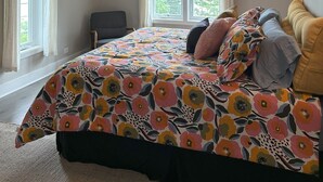 A bedroom with a large bed, a ceiling fan, and two windows with curtains.