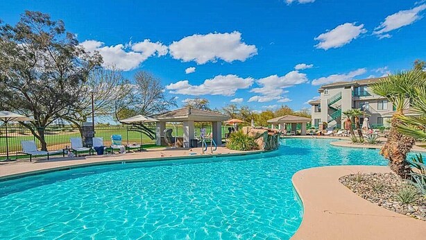 Una piscina con lettini e un gazebo, circondata da edifici e alberi.