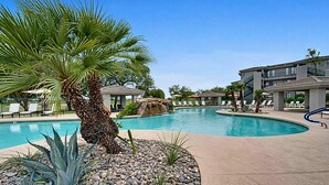 A pool area with palm trees, lounge chairs, and a building with balconies.