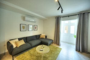 Ein modernes Wohnzimmer mit einem Ecksofa, einem runden Couchtisch und einem großen Fenster mit Vorhängen.