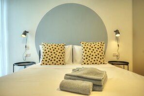 Ein ordentlich bezogenes Bett mit gepunkteten Kissen, zwei Nachttische mit Lampen und ein großer, runder Wandbogen darüber.