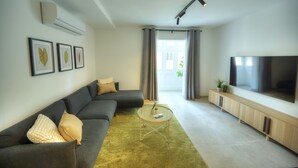 A modern living room with a grey sofa, a round coffee table, and a TV on a wooden cabinet. - Chic, bright and modern 3 bedrooms KBAS1-1 (Gzira)