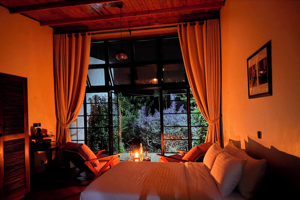 Um quarto aconchegante com uma cama grande, uma mesa com velas e vista para o verde lá fora.