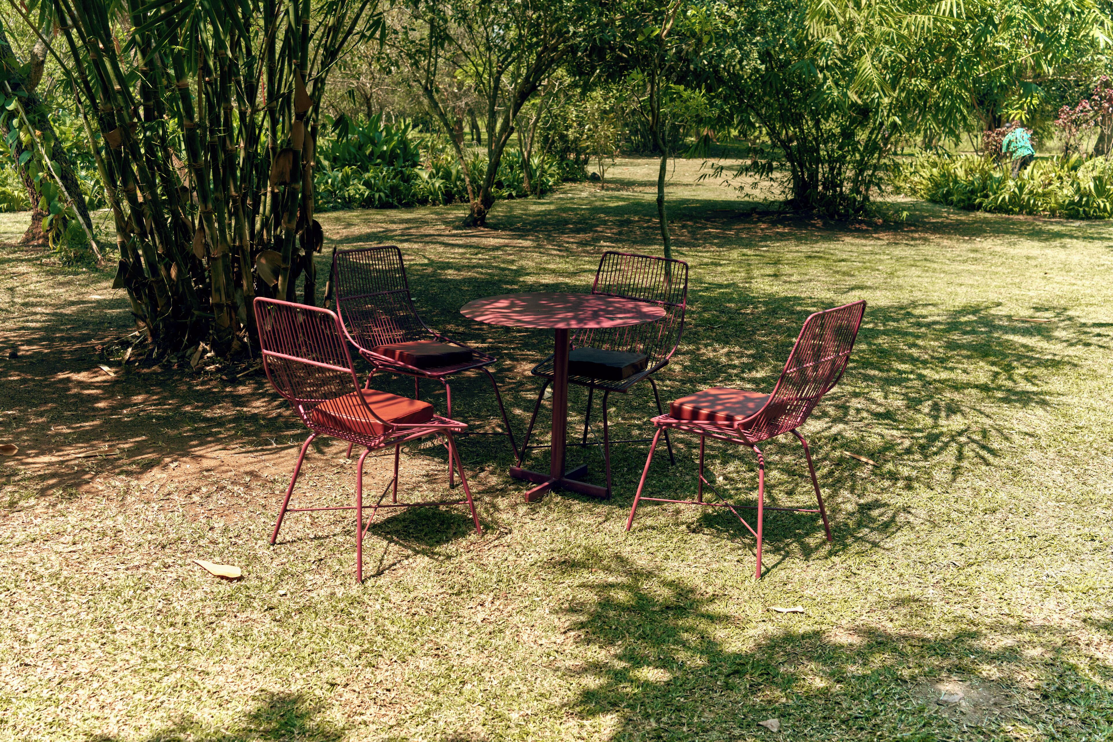 A round table with four red chairs in a grassy outdoor area with trees.