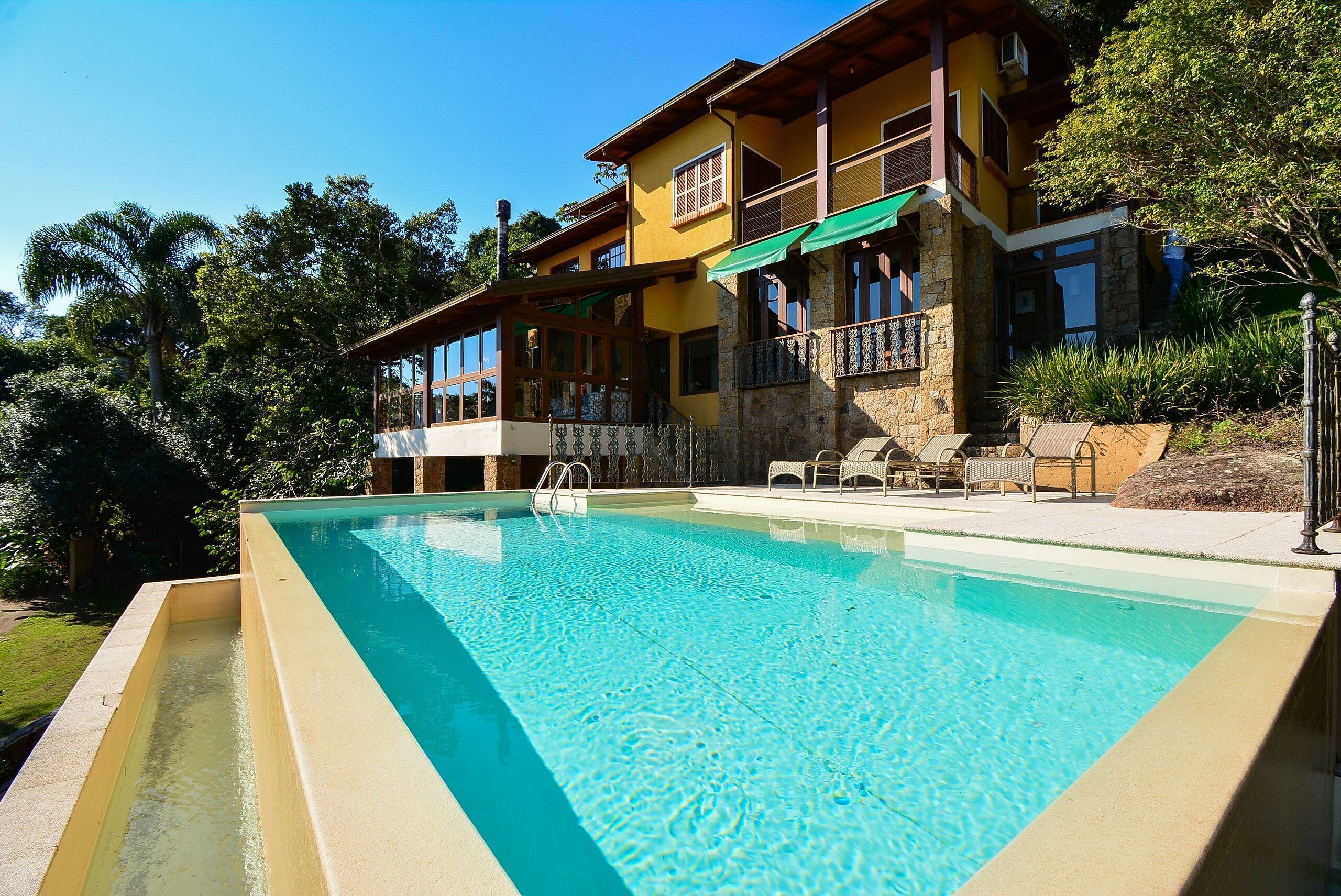 A two-story house with a swimming pool, a balcony, and a patio area with outdoor furniture.