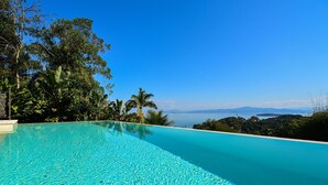 En vacker, turkosblå infinitypool med utsikt över havet och avlägsna berg.