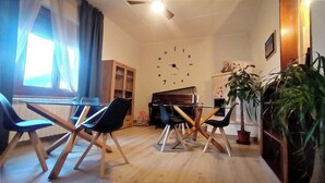 A living room with a piano, a clock on the wall, and a large plant.