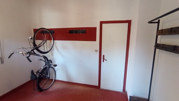 Una habitación con piso rojo, una puerta blanca con marco rojo y una bicicleta montada en la pared.