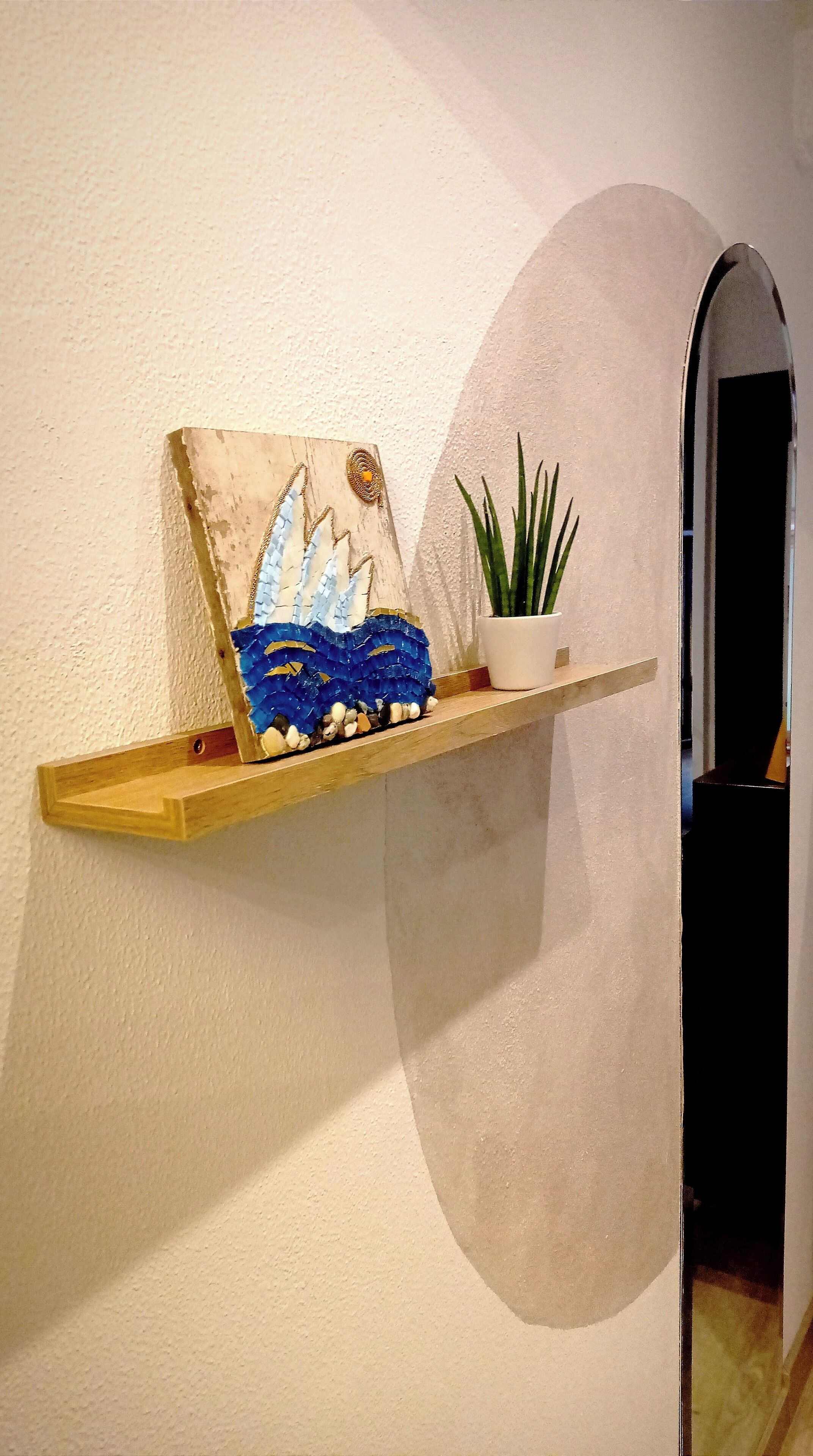 A wooden shelf with a painting and a potted plant against a textured wall.