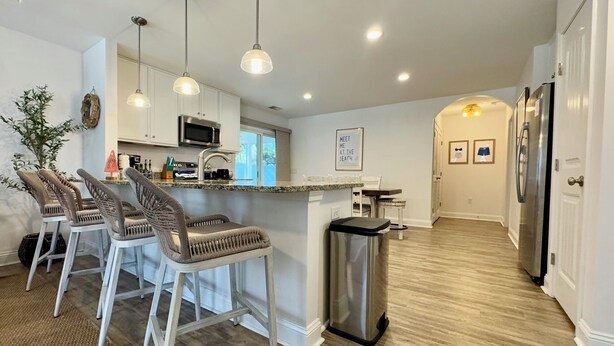 Una cocina moderna con taburetes de bar, un refrigerador de acero inoxidable e iluminación colgante.
