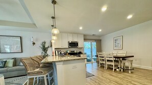 Una cocina moderna con una isla central, muebles blancos y una zona de comedor con una mesa y sillas de madera.