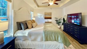 Un dormitorio con cama, ventilador de techo, televisor y ventana.