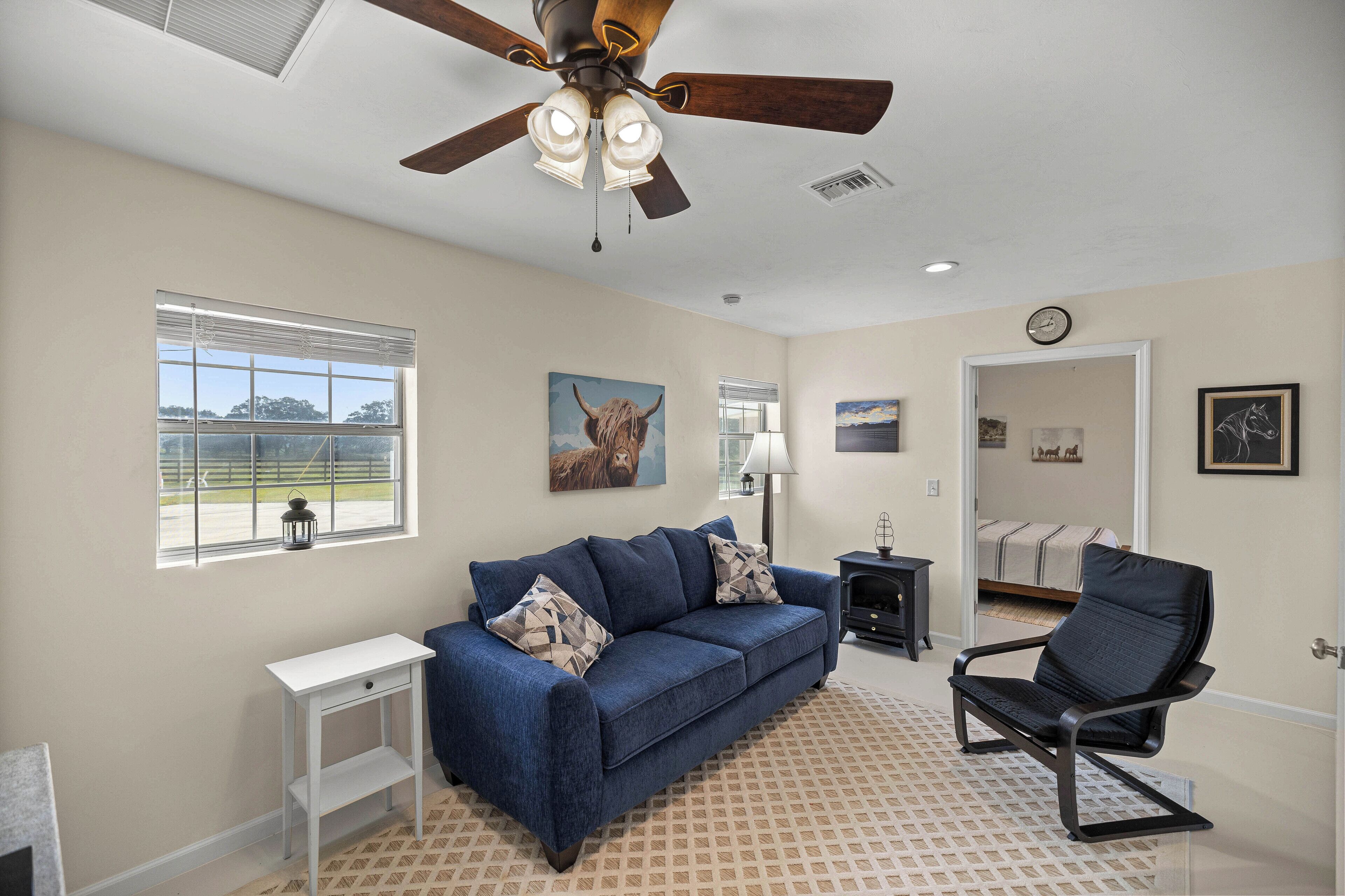 A spacious living room with a blue sofa, a black chair, a white side table, and a ceiling fan.