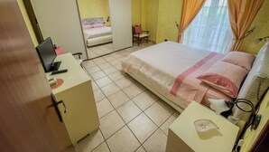 A bedroom with a bed, a desk, a chair, a mirror, and a window with curtains.