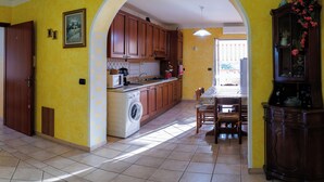 A kitchen with wooden cabinets, a washing machine, and a dining area with a table and chairs.