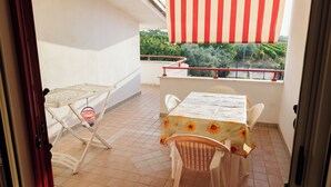 A balcony with a table and chairs, a striped awning, and a view of greenery.