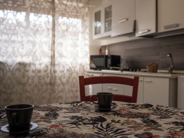 A dining area with a table set for two, a chair, a coffee cup, and a microwave in the background.