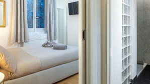 A bedroom with a bed, a window with curtains, a radiator, and a TV mounted on the wall.
