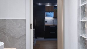 A narrow hallway leading to a modern kitchen with dark cabinetry and a wooden countertop.