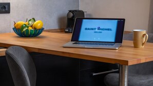 A laptop on a wooden table with a bowl of lemons and a mug.