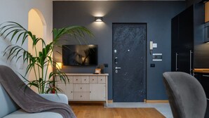 A modern living room with a flat-screen TV, a dark door, and a light-colored sofa.
