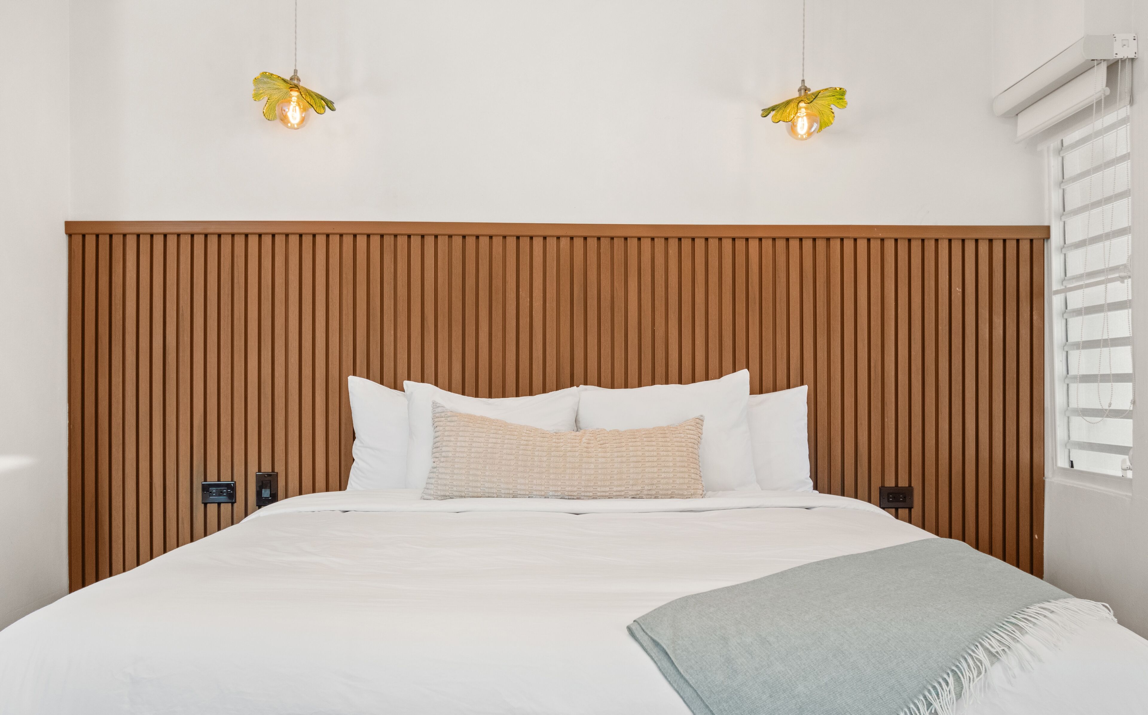 A bedroom with a wooden headboard, white bedding, a light blue throw blanket, and two wall-mounted lamps.