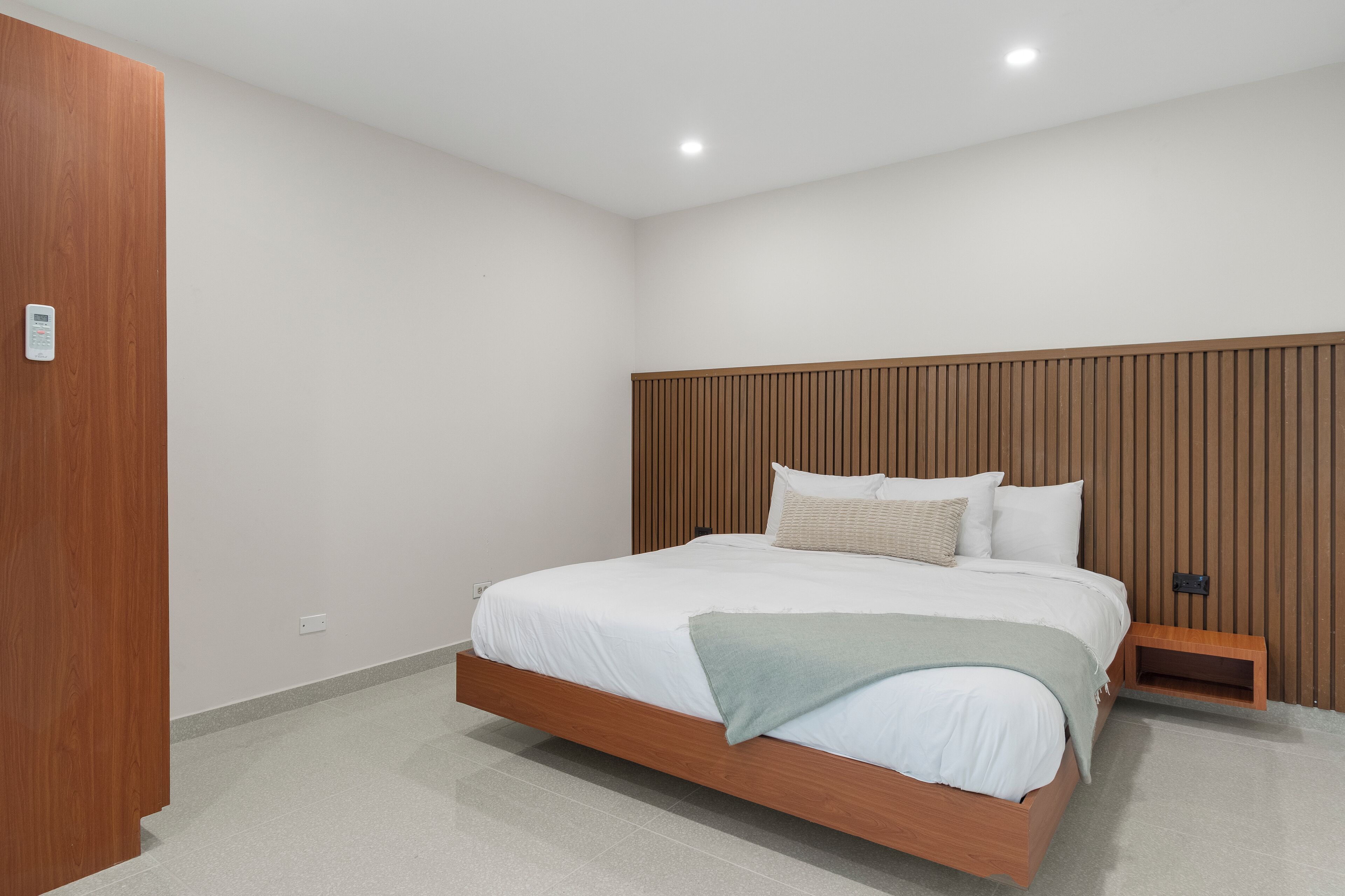 Un dormitorio moderno con estructura de cama de madera, ropa de cama blanca y cabecera de madera.